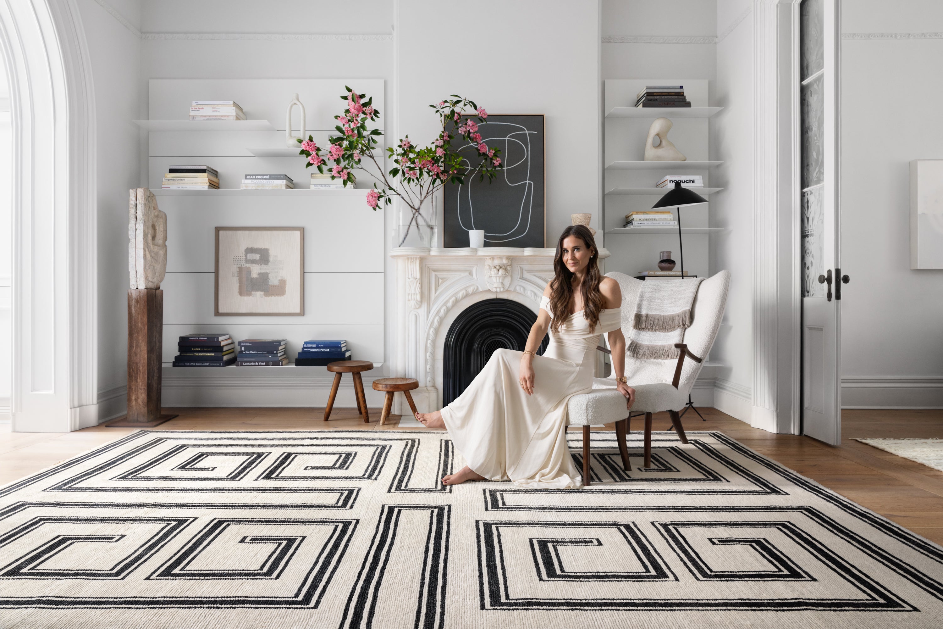 Ashley Stark sitting in a elegantly designed room with a large geometric designed rug, featuring white and black design elements.