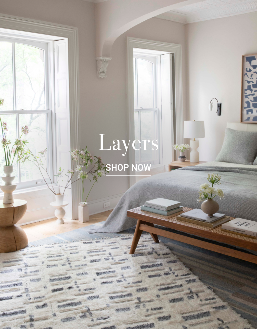 Traditional bedroom scene with bed, end table and design rug.
TEXT overlay in white: "Layers" with SHOP NOW below it.