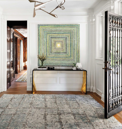 Artistic entryway to a home with a large designer rug and green geometric art on a white wall.